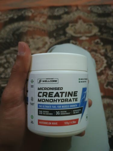Reviewer holding a white tub of Wellcore Micronised Creatine Monohydrate in the Watermelon Wave flavor.