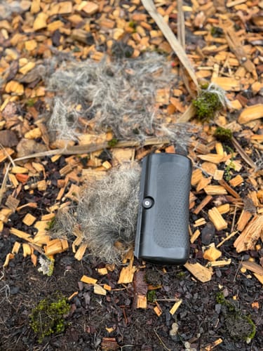 Rezensent zeigt die Fellwunder Bürste neben zwei großen Haufen entferntem Unterfell auf Holzschnitzeln.