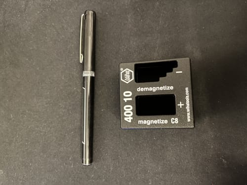 Reviewer's black Wiha 40010 Magnetizer and Demagnetizer on a dark surface, shown next to a pen for size comparison.