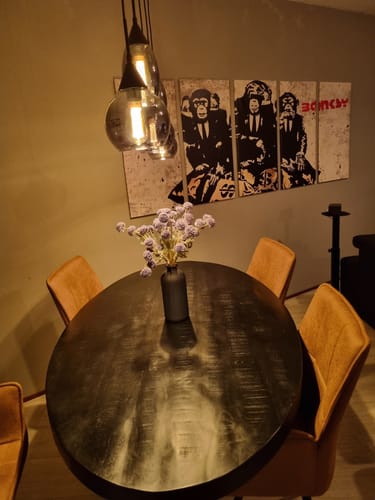 Beoordelaar toont de matzwarte Balim Vaas met kunstbloemen op een donkere, houten eettafel.