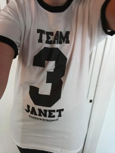 Customer wearing the white Team Janet Three's Company Ringer Shirt with black text and trim.