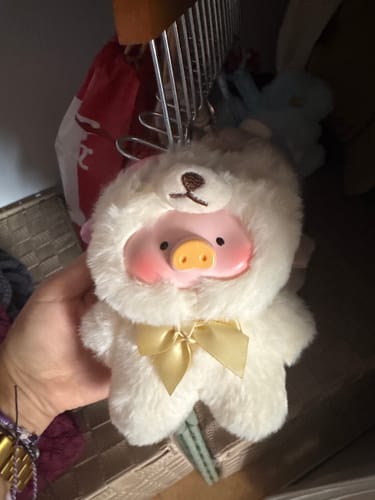 Customer holding the Lulu The Piggy plush pendant, showing the pig in a fluffy white teddy costume with a yellow bow.