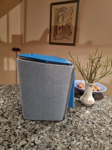 Ein Kunde zeigt seine KINI Filterkanne mit grauer Filzhülle und blauem Deckel auf einer Arbeitsplatte.