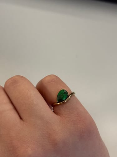 Close-up of a reviewer wearing the Pia Birthstone Ring with a green pear-cut stone and gold wave band.