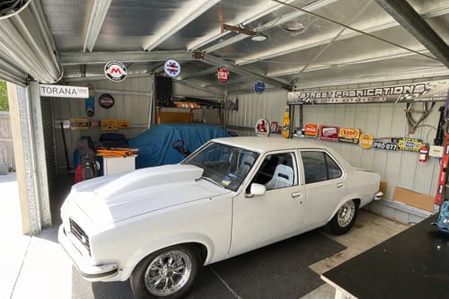 Customer's Motion Companies metal sign set hanging from the ceiling in a garage with a classic white car.