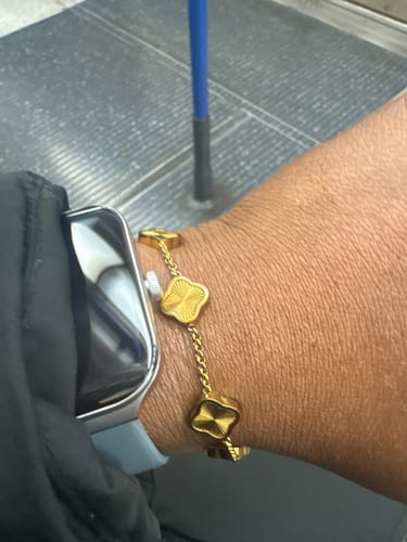 A reviewer shows their gold-colored bracelet with clover-shaped charms on their wrist.
