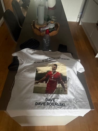 A reviewer's custom-printed white Super-soft Heavy Tee featuring a photo of a person and text, laid flat on a table.