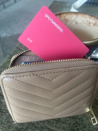 Customer's pink SPOTMINDERS tracking card sticking out of a beige, quilted zippered wallet.