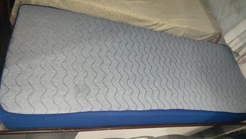 Customer's Flo Mattress Ortho on a bed, showing its grey wavy-patterned top and blue sides.