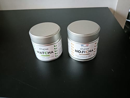 Client montrant les boîtes de THÉ HOJICHA BIO et de thé Matcha sur une table noire.