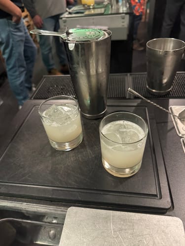 Rezensent zeigt zwei fertige Cocktails mit GOLDBERG Ginger Beer in Gläsern mit Eis auf einer Bartheke.