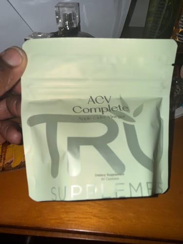Customer holding the light green pouch of ACV Complete supplements on a wooden surface.