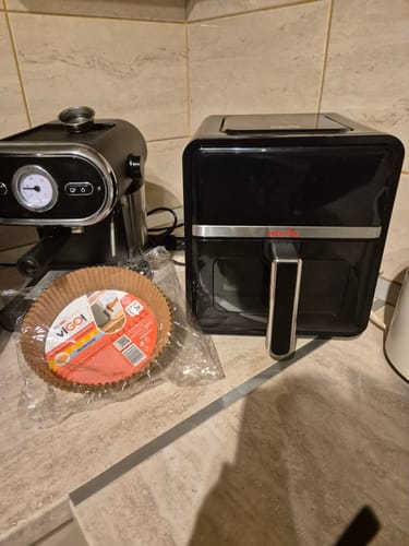 Client arătând friteuza Air Fryer Novio StonePro pe blatul de bucătărie, lângă un espressor.