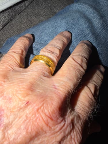 A close-up of a customer's hand wearing the textured, gold Aureum ring against blue jeans.