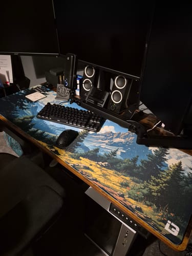 Reviewer's Alpine Landscape desk pad on a desk with a keyboard, mouse, and speakers.