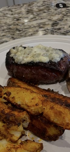 Customer's cooked USDA Choice Top Sirloin with a cheese topping, served with seasoned potato wedges on a plate.