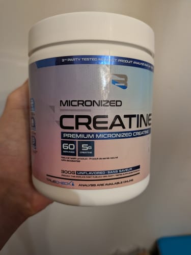 Un client tient le pot blanc de Créatine Micronisée de Believe dans sa main.