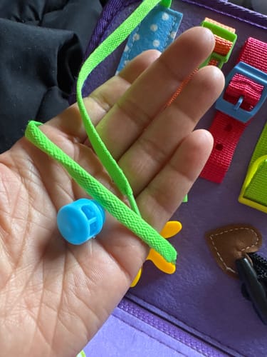 Customer's hand holding a detached blue toggle and green lace from the TibaKids Educational Activity Pack.