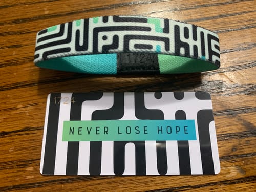 Customer's Never Lose Hope Bracelet with its maze-patterned exterior next to the matching collector card on a wood table.