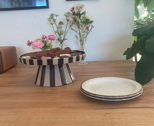 Recensent toont de gestreepte by fonQ Arcade serveerschaal op een houten tafel, gevuld met chocolaatjes.