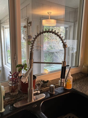 Reviewer's Spiro Dual Handle Kitchen Faucet installed on a black double sink, shown in a kitchen setting.