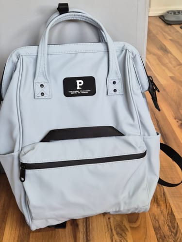 Reviewer's light gray Cascade Backpack on a wood floor, propped against a gray piece of furniture.