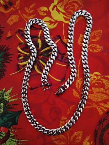 Un cliente muestra la brillante Cadena Cuban Link sobre un fondo rojo decorativo.