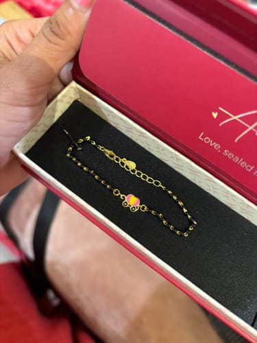 Reviewer showing the Golden Fairy Tale Infant Bracelet with black beads and a carriage charm inside its red and cream box.