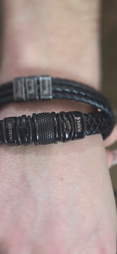 Close-up of a reviewer's wrist wearing the personalized black Titan bracelet with the names 'Dorian' and 'Nadia' on the beads.