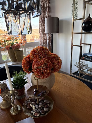 Klant toont de grote oranje zijden hortensia's in een vaas op een eettafel.