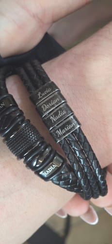 Customer wearing two personalized black bracelets on one wrist, showing engraved names like Lucia, Dorian, and Nadia.