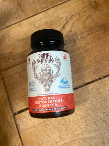 Reviewer's bottle of Primal Viking Natural Testosterone Booster supplement on a wooden surface.