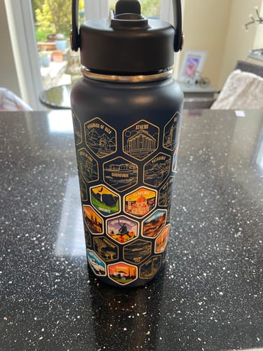 Customer's black World Explorer Bottle on a counter, with several colorful travel stickers applied over the destination engravings.