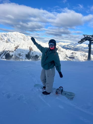 Reviewer wearing the oversized army green snow jacket while on a snowboard on a snowy mountain.