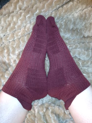 Recensent visar sina fötter i ett par vinröda ankelstödstrumpor mot en mjuk filt.