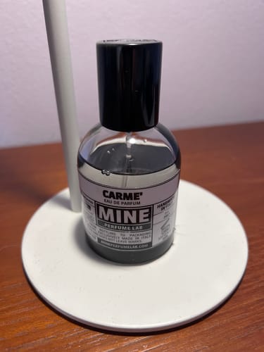 Il profumo CARME' di un recensore in un flacone trasparente con tappo nero, posizionato su un supporto bianco.