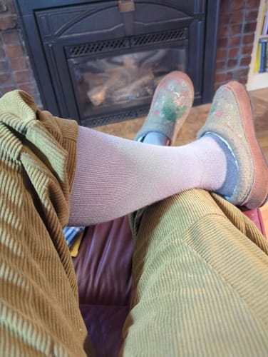 A customer relaxing by a fireplace, wearing light-colored Performance Eucalyptus Compression Socks.
