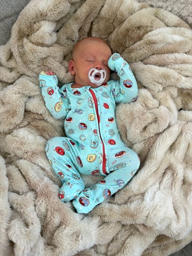 Customer's newborn baby sleeping on a fluffy blanket while wearing the Blue Space Donut Bamboo Convertible Footie.