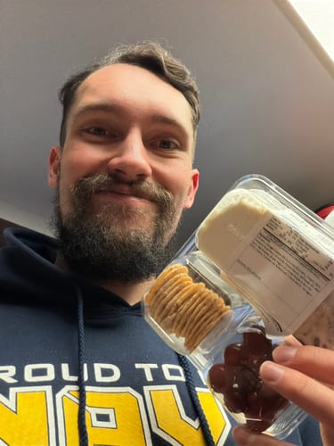 A reviewer holds up the Protein Snack Pack, showing crackers and grapes in the clear compartmentalized container.