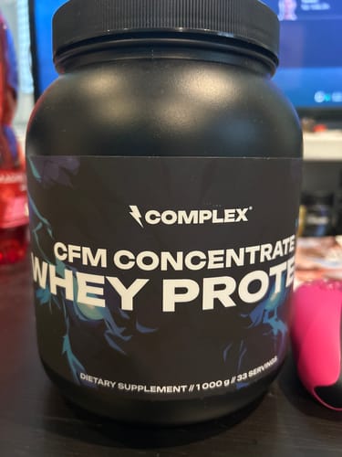 Customer's large black tub of Complex CFM Concentrate Whey Protein on a desk.