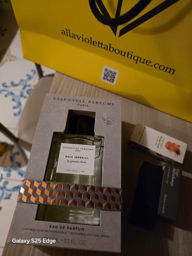Cliente mostra il profumo Bois Imperial nella sua confezione, con campioni gratuiti e la borsa di una boutique.