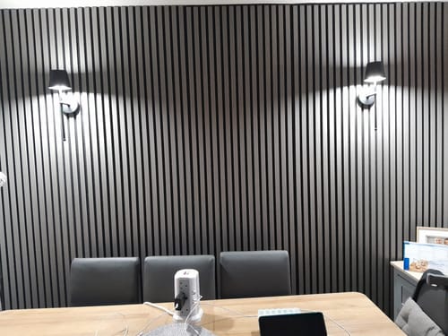 Customer's dark Premium Acoustic Slatted Wall Panels installed on a feature wall, lit by two wall sconces.