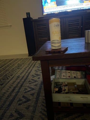 Customer's yellow and white can of Pina Colada Kava Tonic resting on a wooden coffee table.