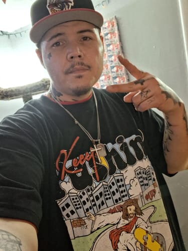 A reviewer posing in the black "Jesus Keeps Pushin" T-Shirt, showing the colorful front graphic.
