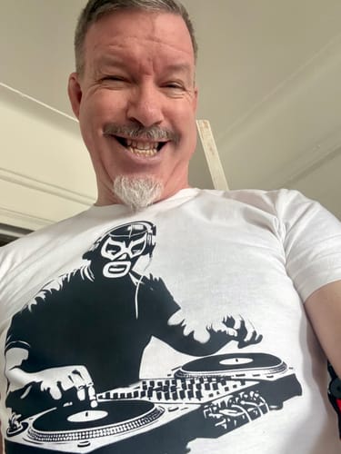 Close-up of a reviewer smiling while wearing the white Lucha DJ Art De La Calle™ T-Shirt.