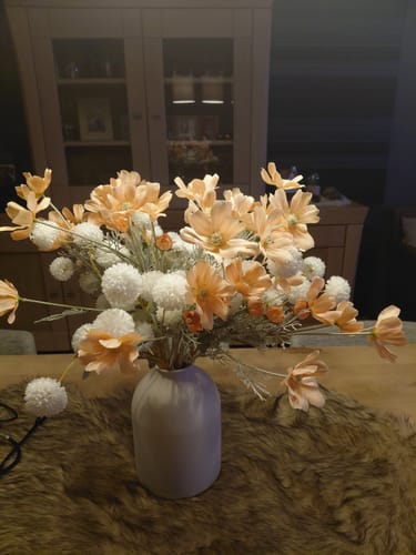 Recensent toont de matte witte Casa vaas op een tafel, gevuld met een groot boeket kunstbloemen.