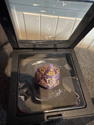 Customer's personalized purple D20 dice in a display case, showing the custom engraved initials and date on its 20-face.
