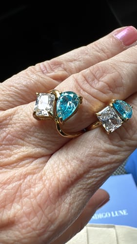 Close-up of a reviewer's hand wearing two gold Navae Birthstone Rings with clear and light blue stones.