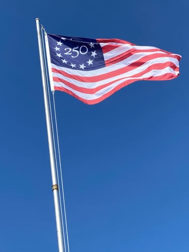Customer's photo of a special American flag with '250' on it, flying on a pole against a clear sky.