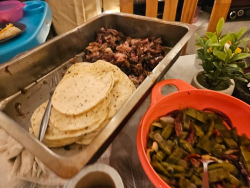Cliente mostrando las costillas short rib deshebradas en una bandeja de metal junto a tortillas y una guarnición.